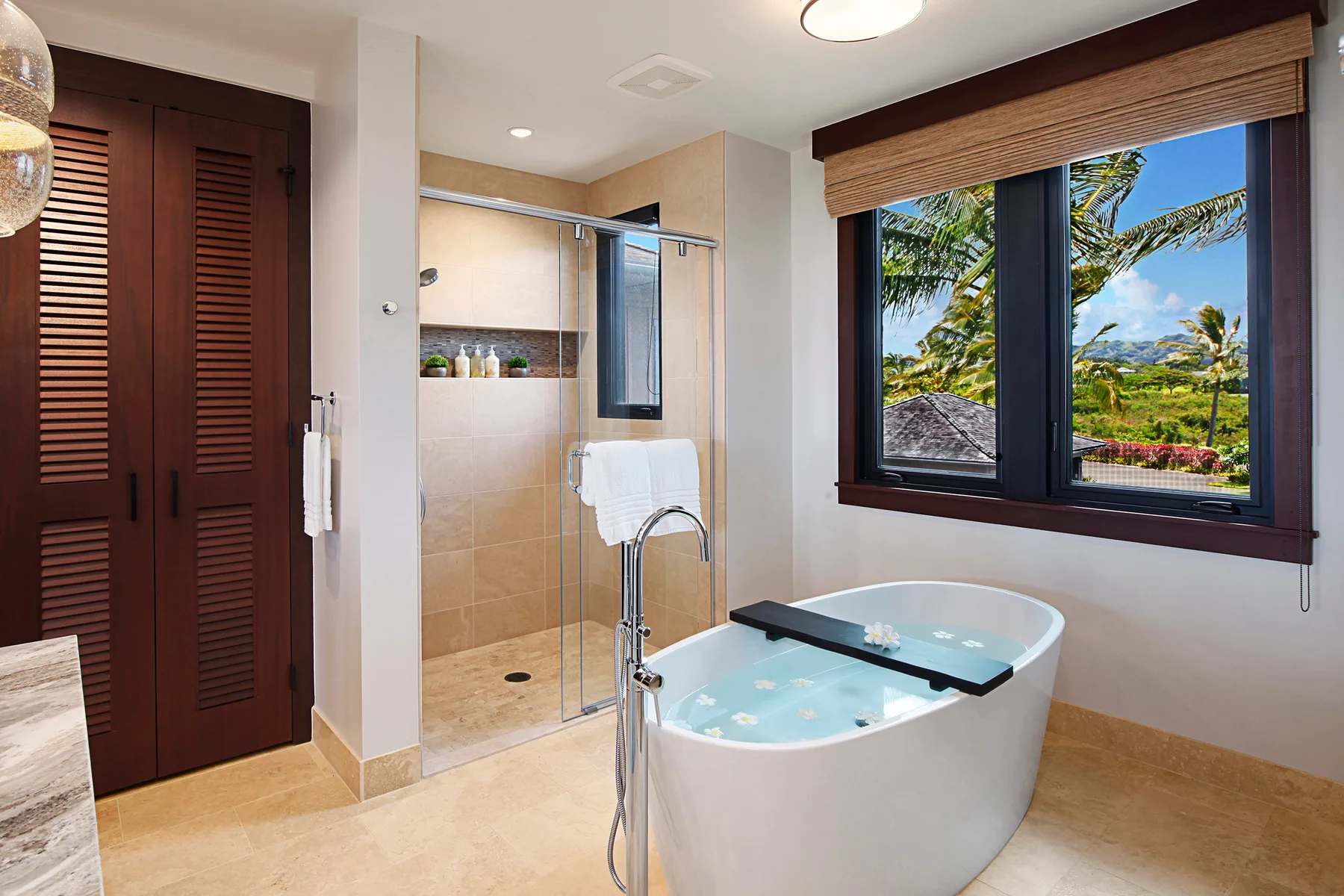 A bathroom with a bathtub, glass shower, and large window overlooking greenery.