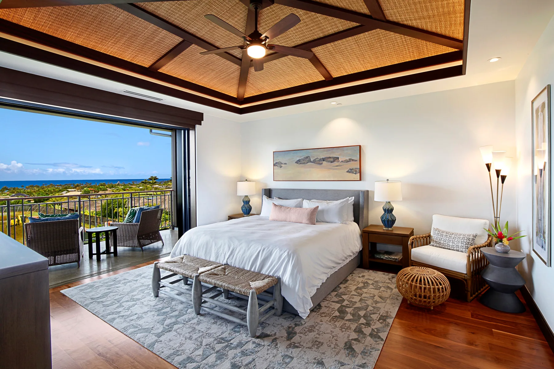 A bedroom with a large bed, woven ceiling, and open balcony overlooking the ocean.