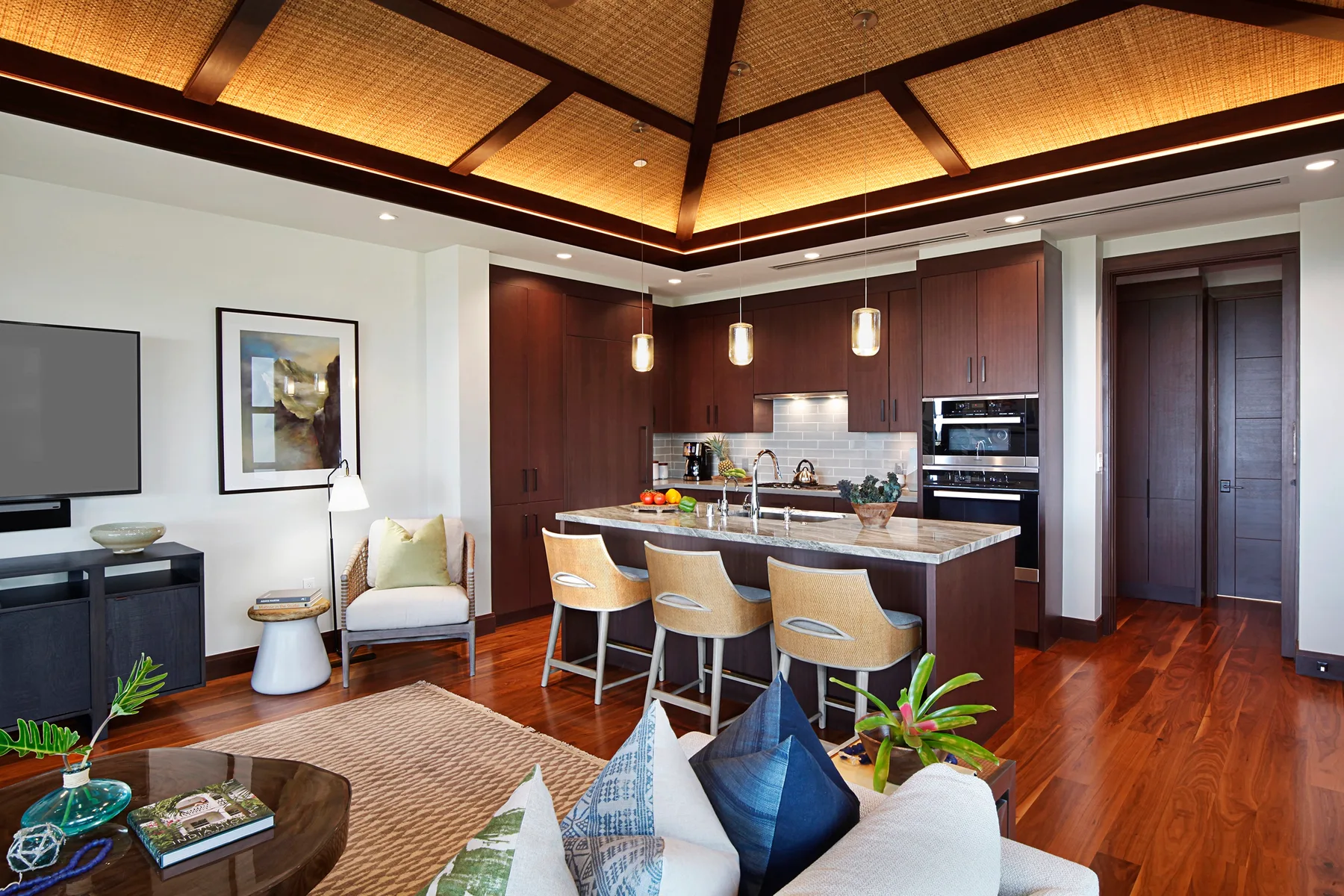 A living room opens onto a kitchen, with a counter and seating beneath a patterned ceiling.