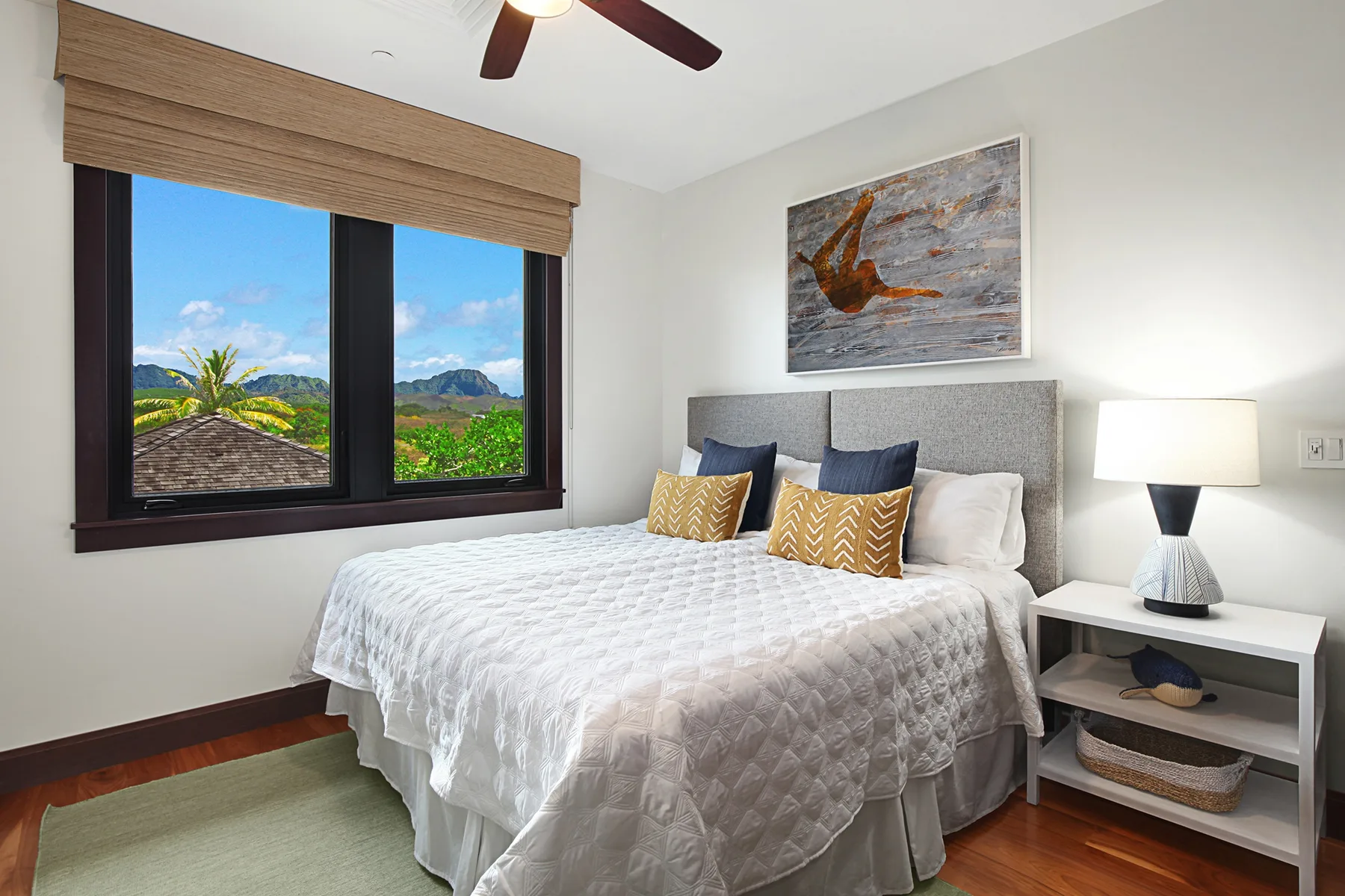 A bedroom with a neatly made bed, bedside table, and window overlooking greenery.