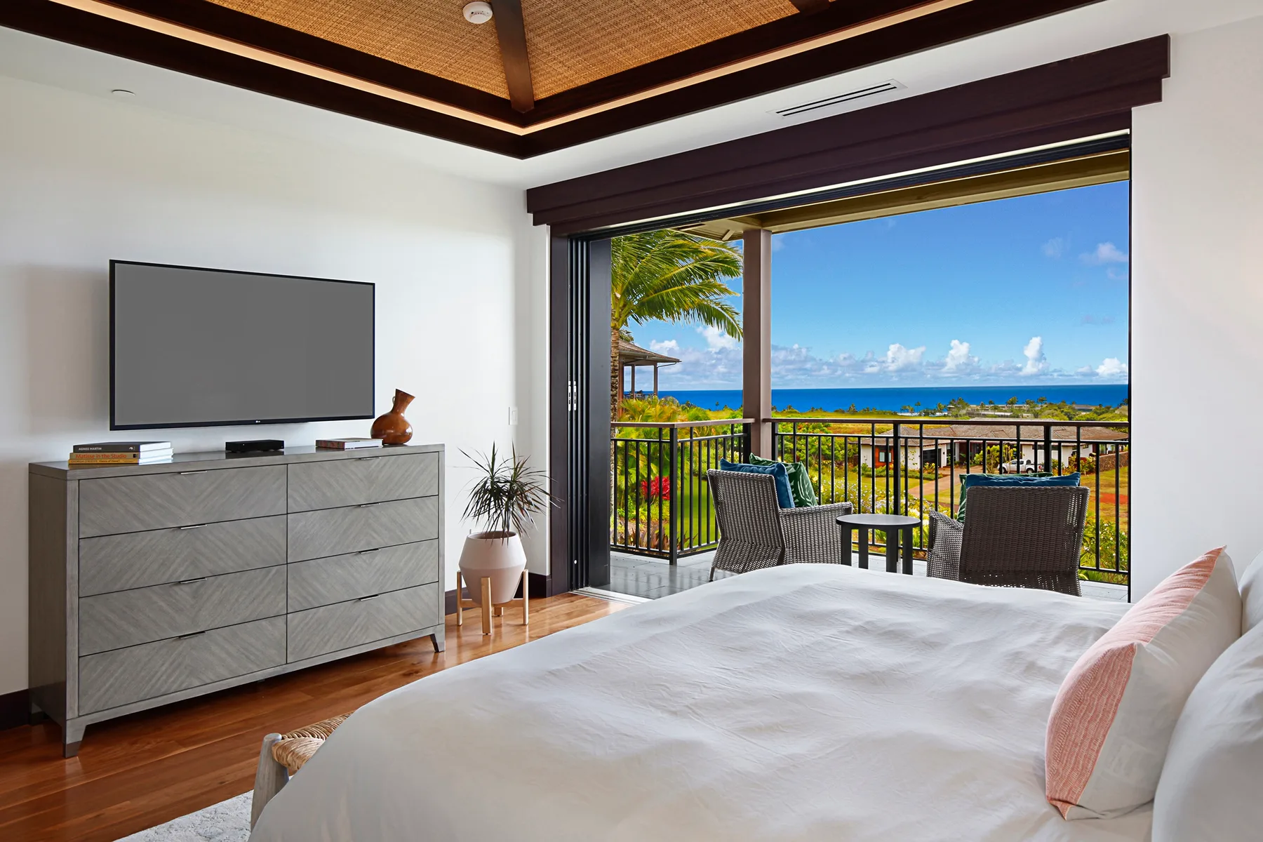 A bright bedroom opens onto a balcony with seating and ocean views.