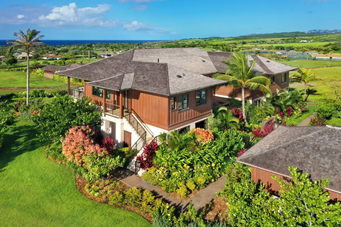 A multi-wing house sits amid landscaped gardens with the ocean visible in the distance.