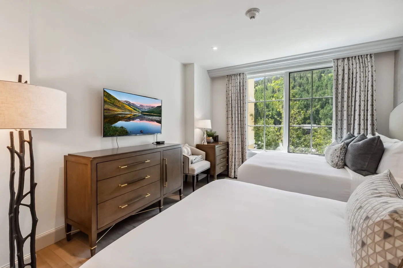 Un dormitorio luminoso con dos camas y una gran ventana con vistas a la vegetación.
