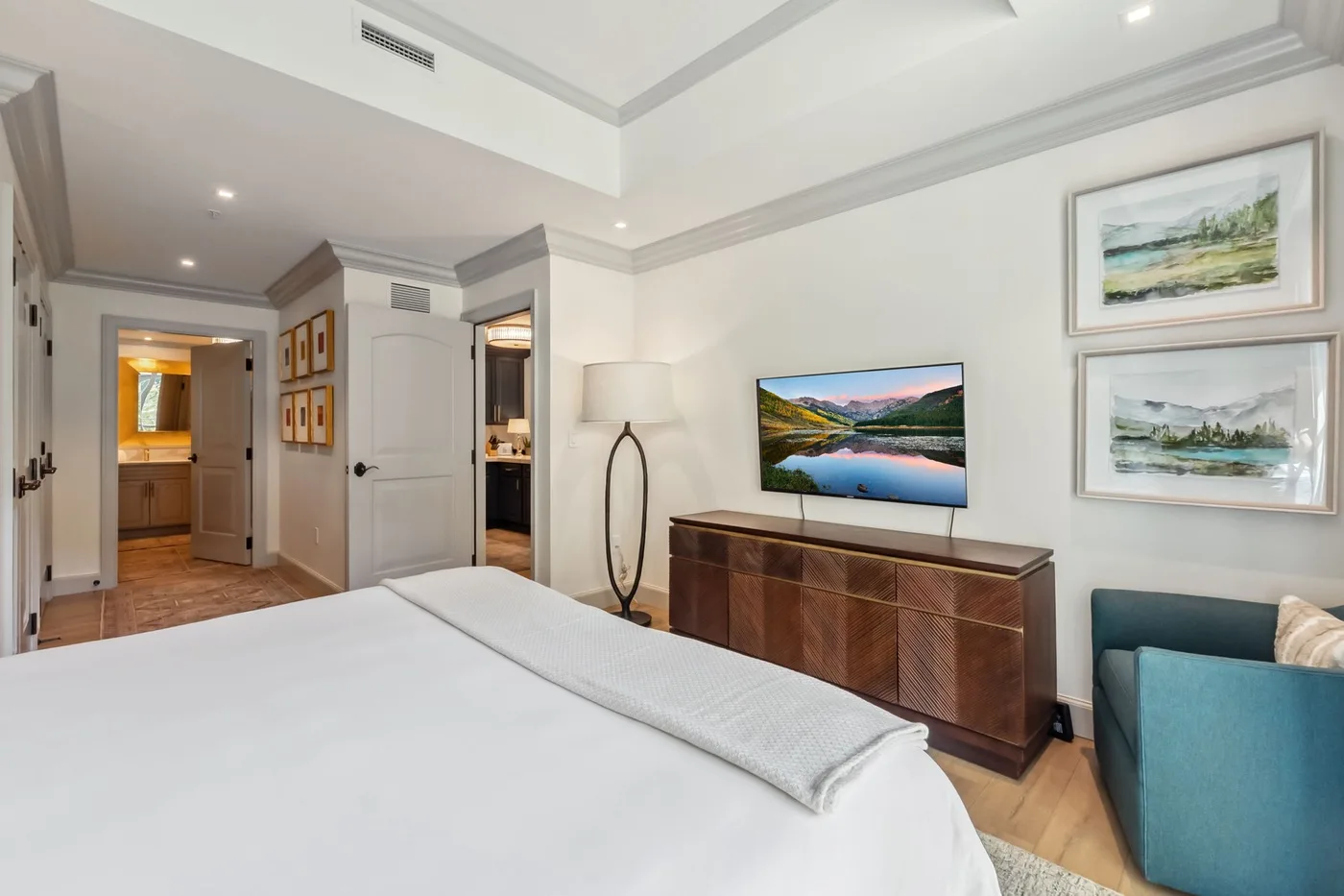 Un dormitorio luminoso con una cama grande, una cómoda y un televisor en la pared.
