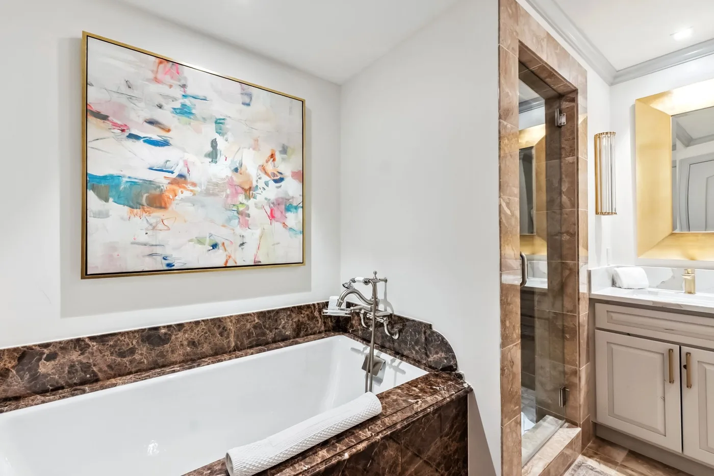Un baño con bañera, revestimiento de aspecto marmóreo y una obra enmarcada.