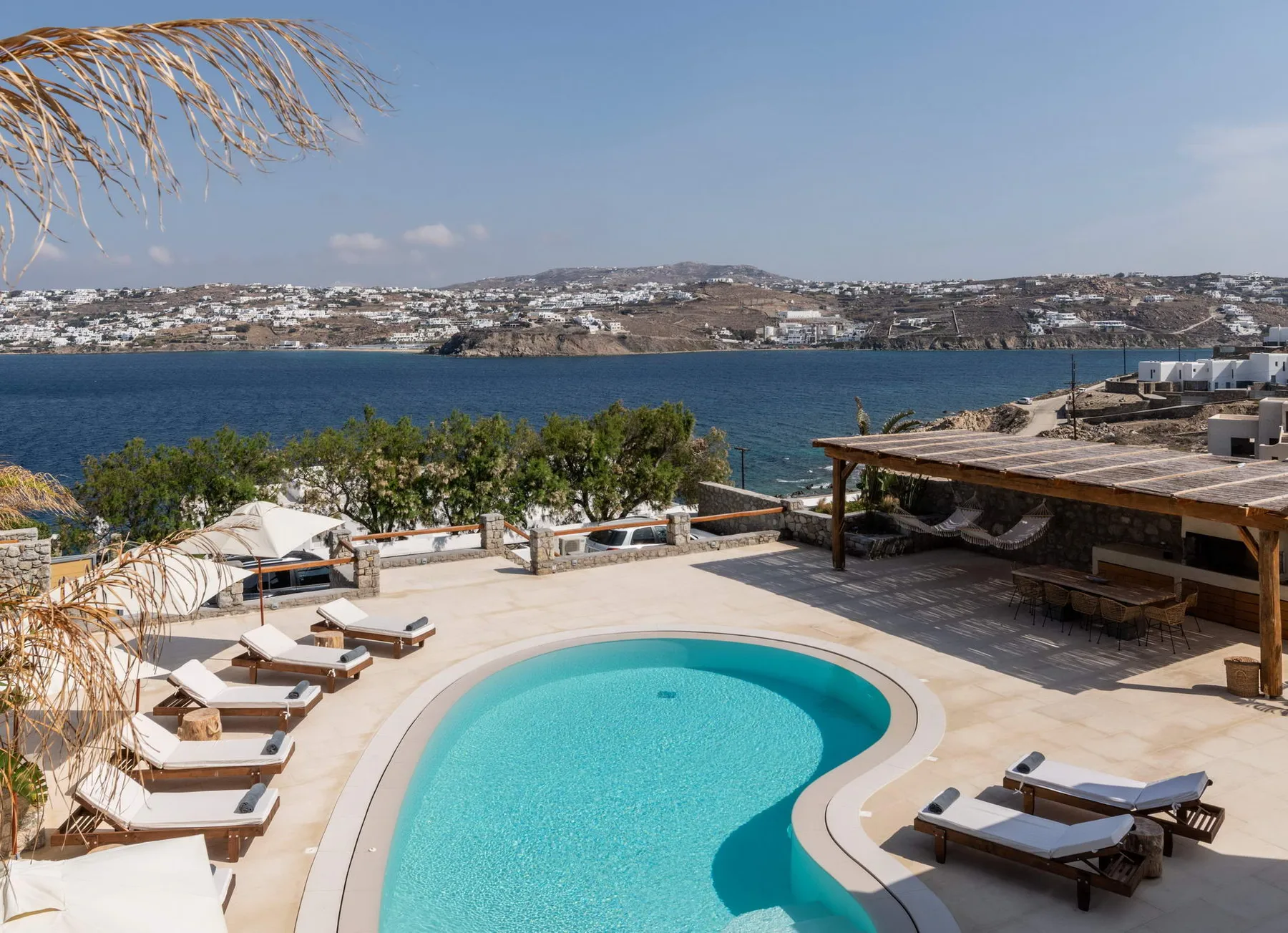 Una terraza junto a la piscina da al mar, con tumbonas y una zona de estar sombreada.