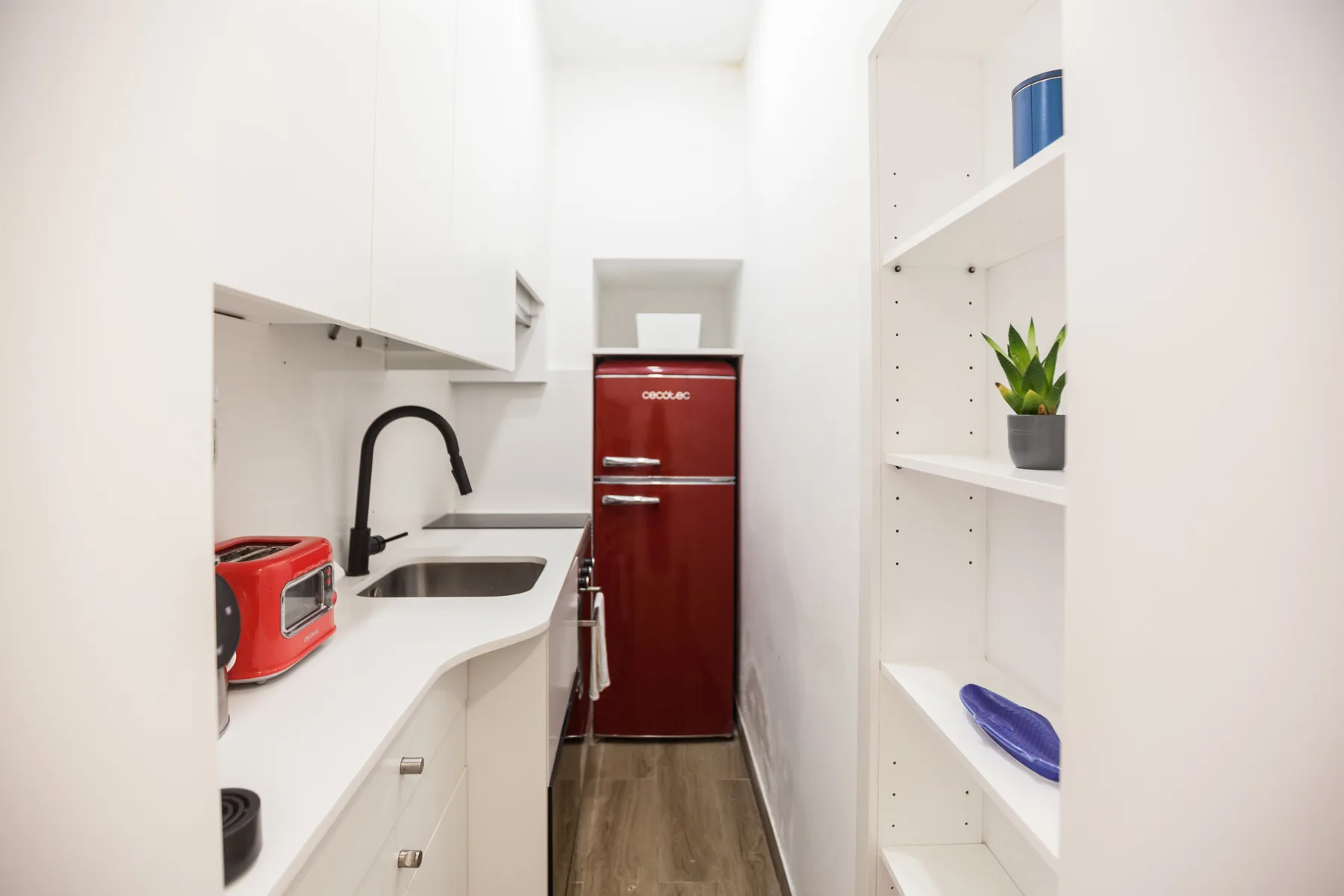 A narrow white kitchen with a red refrigerator and countertop appliances.