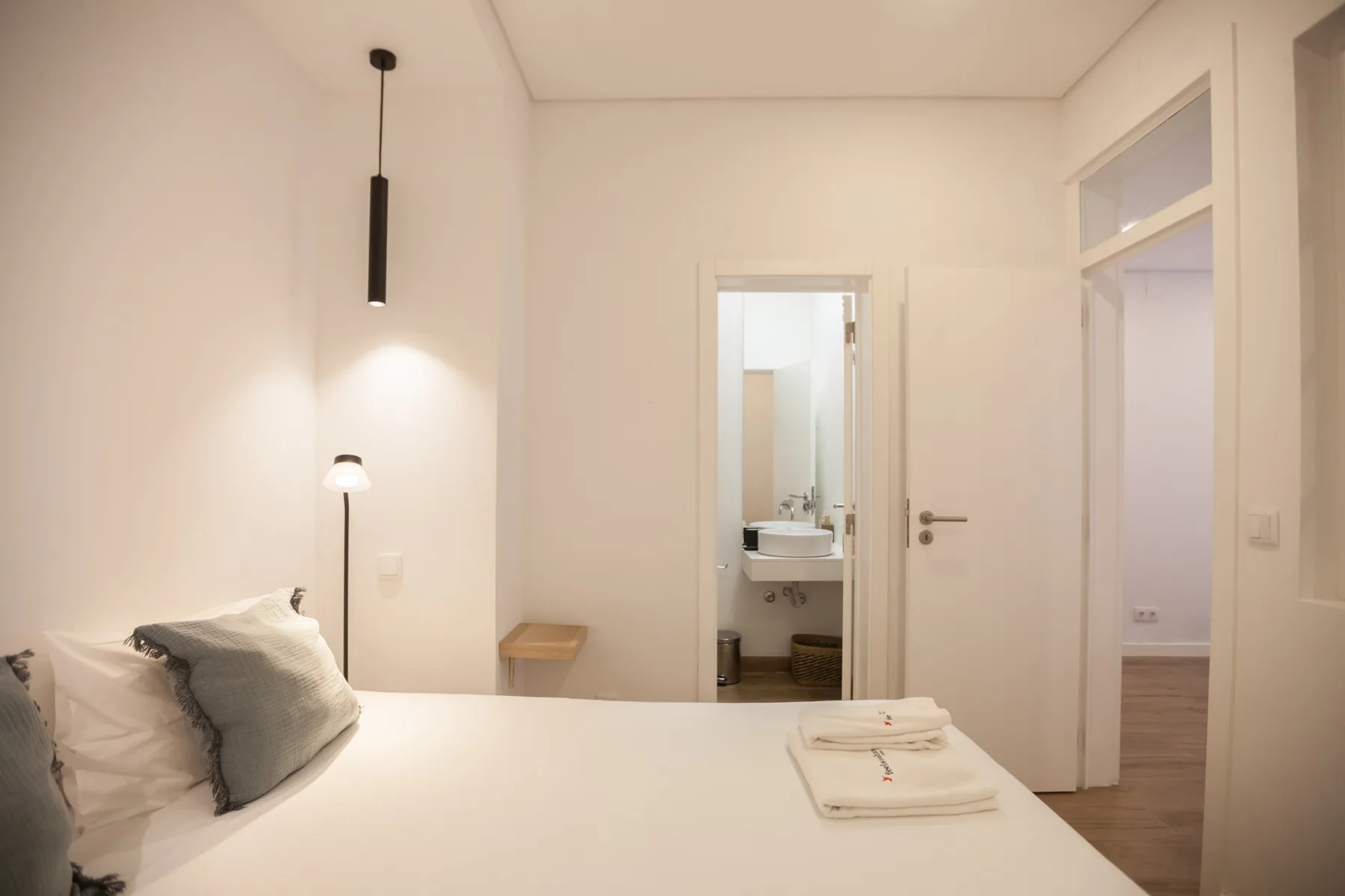 A bright bedroom with a neatly made bed and an open doorway to a washroom.