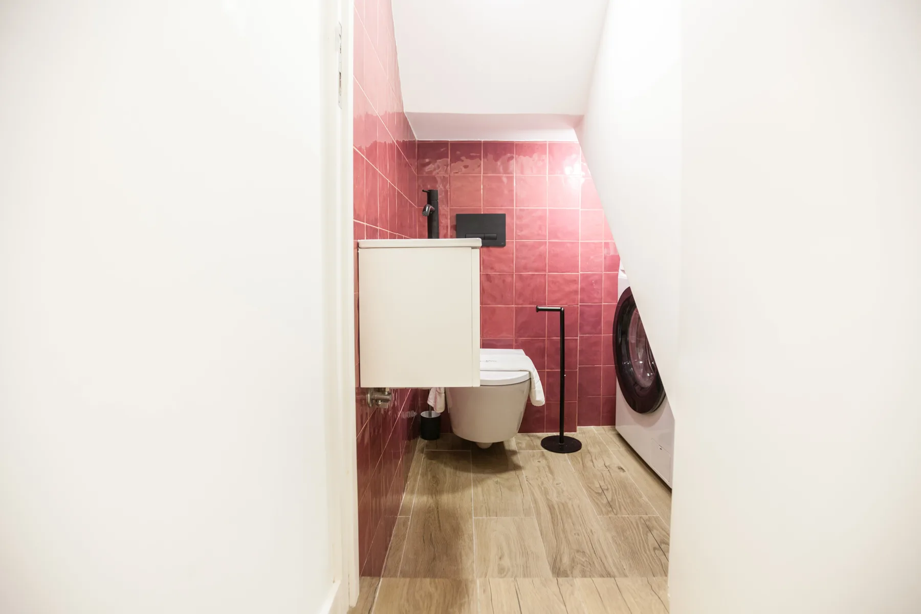 A narrow bathroom with a toilet, sink, and washing machine.
