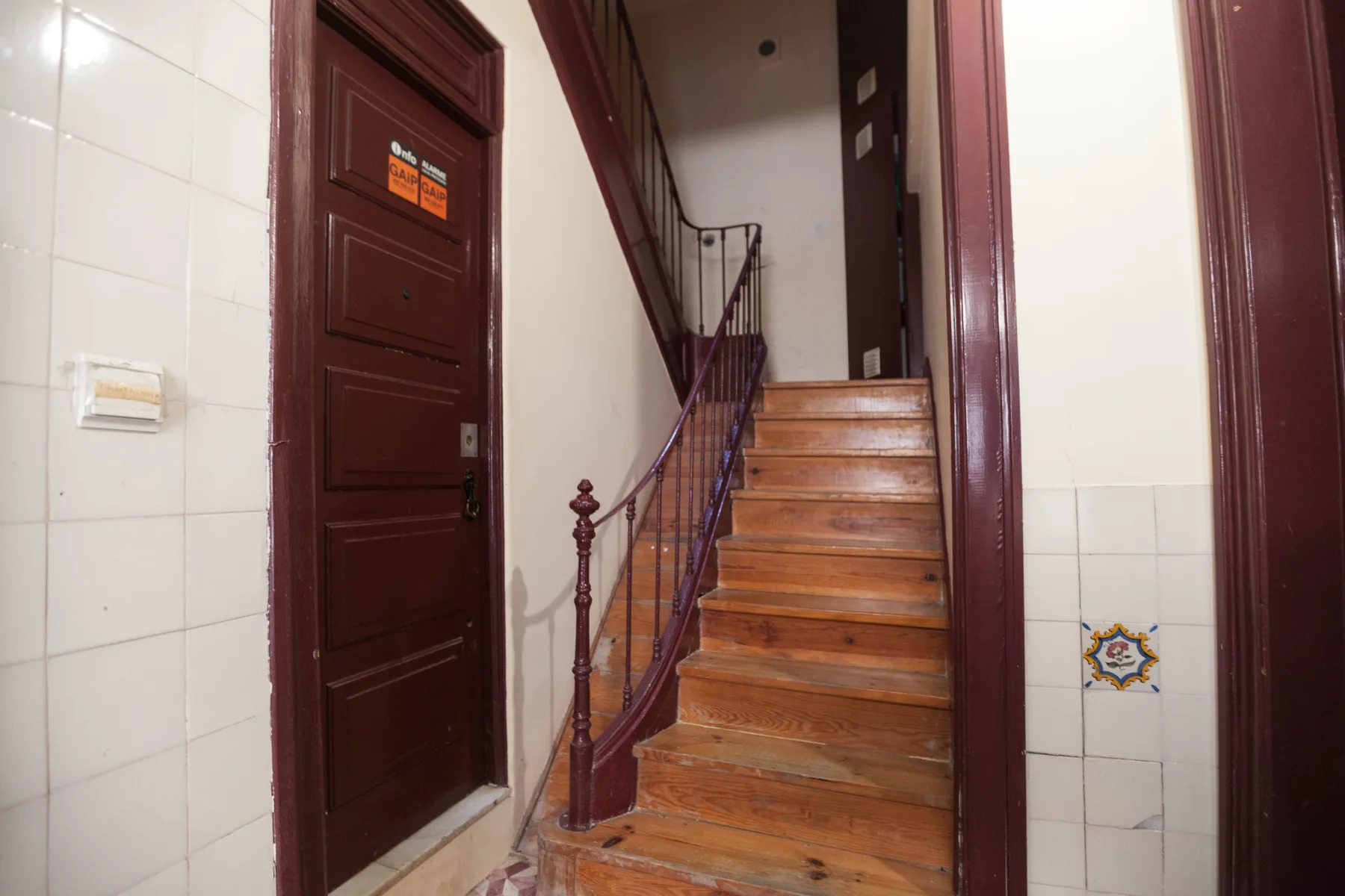 A tiled entry hall with a wooden staircase rising beside a dark doorway.