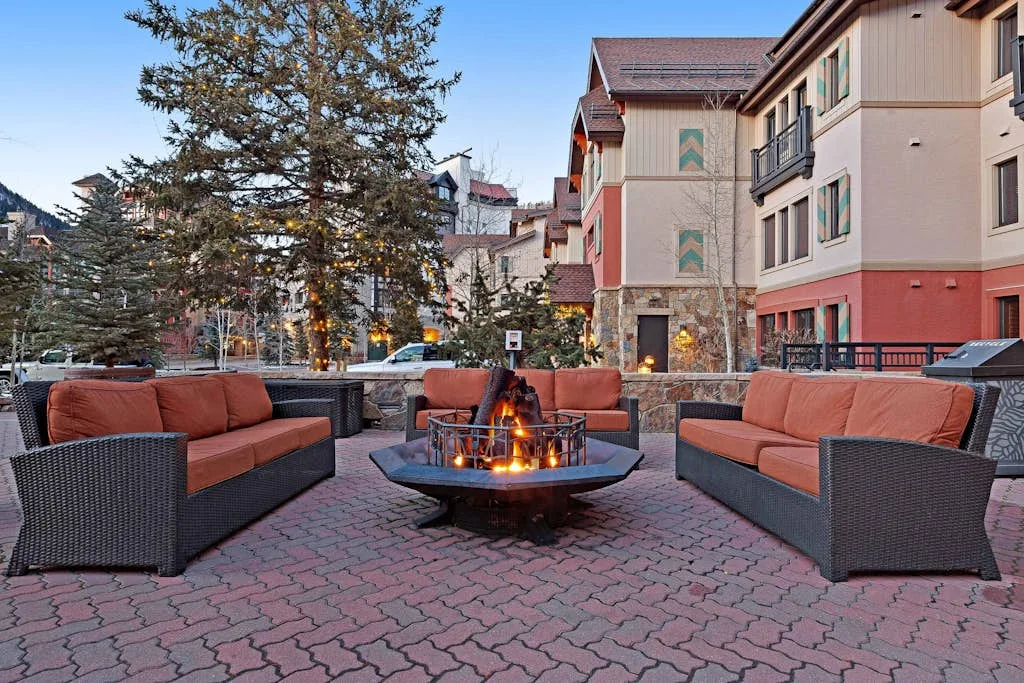 An outdoor seating area surrounds a lit fire pit beside a building.