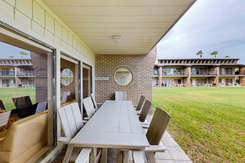 A covered patio with an outdoor dining table overlooks a grassy courtyard.