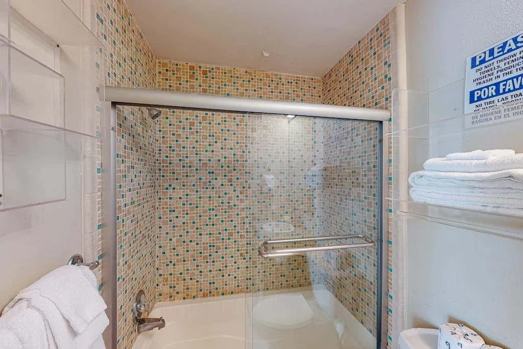 A tiled bathroom shower with a glass screen and folded towels.