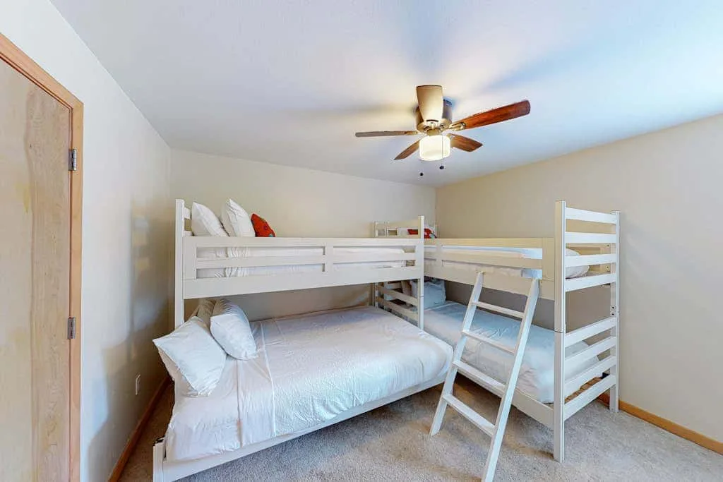 A bedroom with bunk beds and white bedding beneath a ceiling fan.
