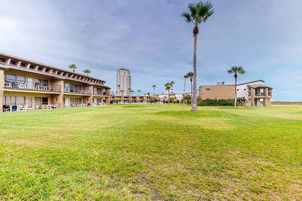 A grassy courtyard lies between low-rise buildings and palm trees.