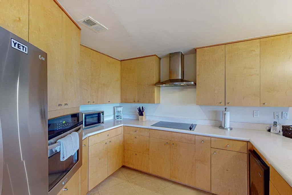 A kitchen with light wood cabinets, a refrigerator, and a cooking range.