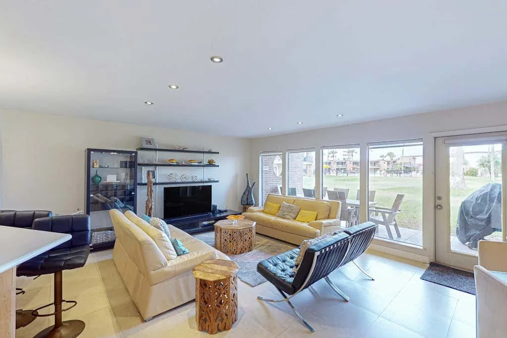 A bright living room with seating, a television, and windows opening onto a patio.