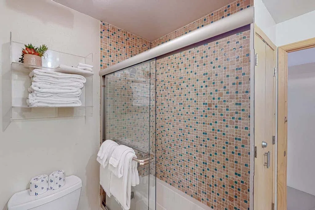 A tiled bathroom shower with towels hanging beside it.