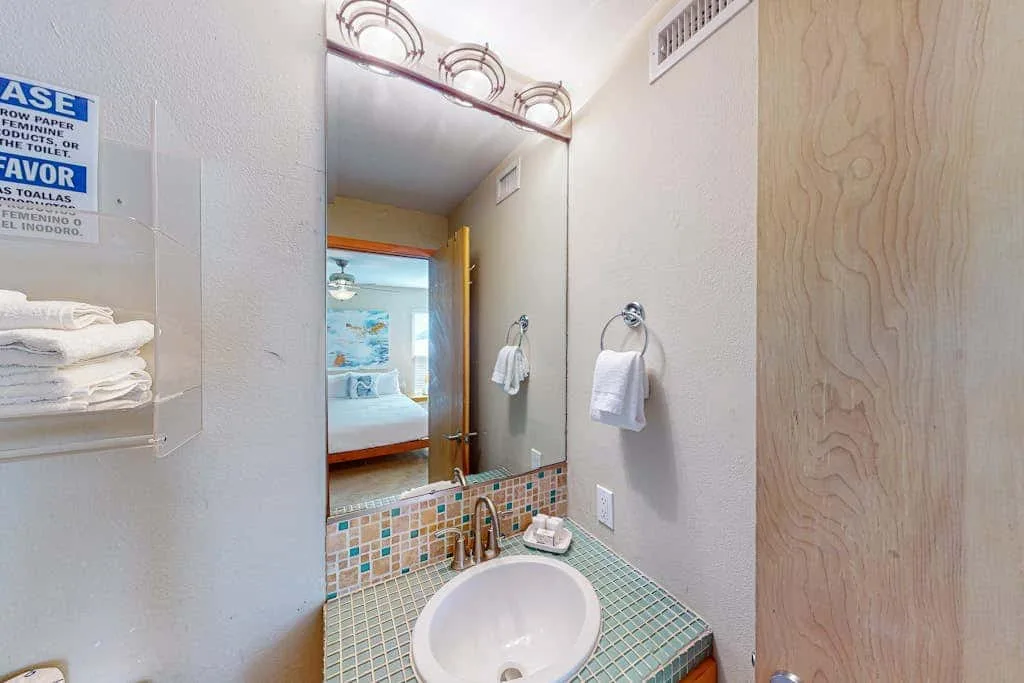 A bathroom vanity with a tiled counter, mirror, and towel rack.