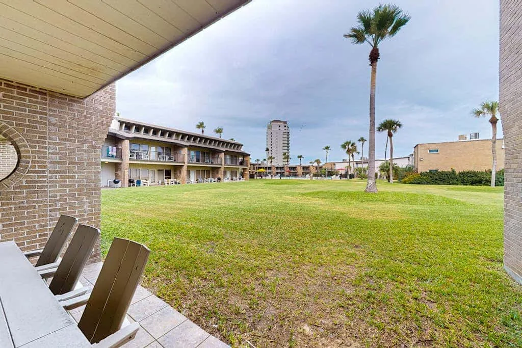 A grassy courtyard with palm trees and resort-style buildings in the background.