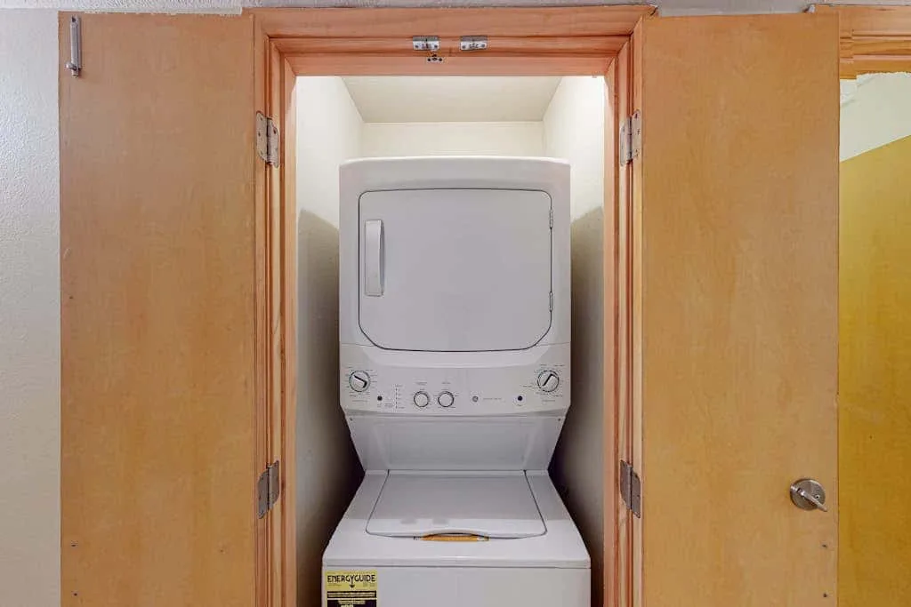 A laundry area with a stacked washer and dryer behind open wooden doors.