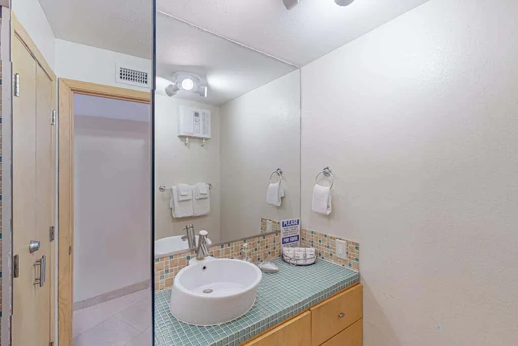 A bathroom vanity with a round basin and tiled countertop.