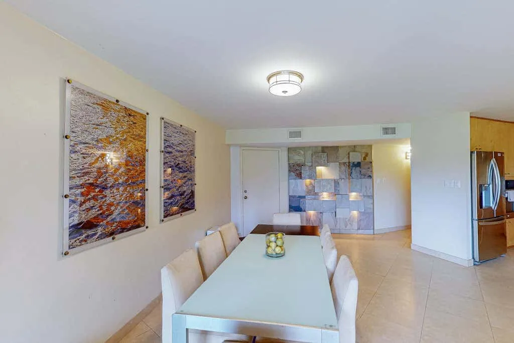 Dining area with a long table, wall art, and a kitchen visible nearby.