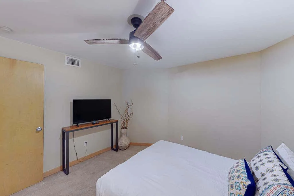 A bedroom with a bed, television on a stand, and ceiling fan.