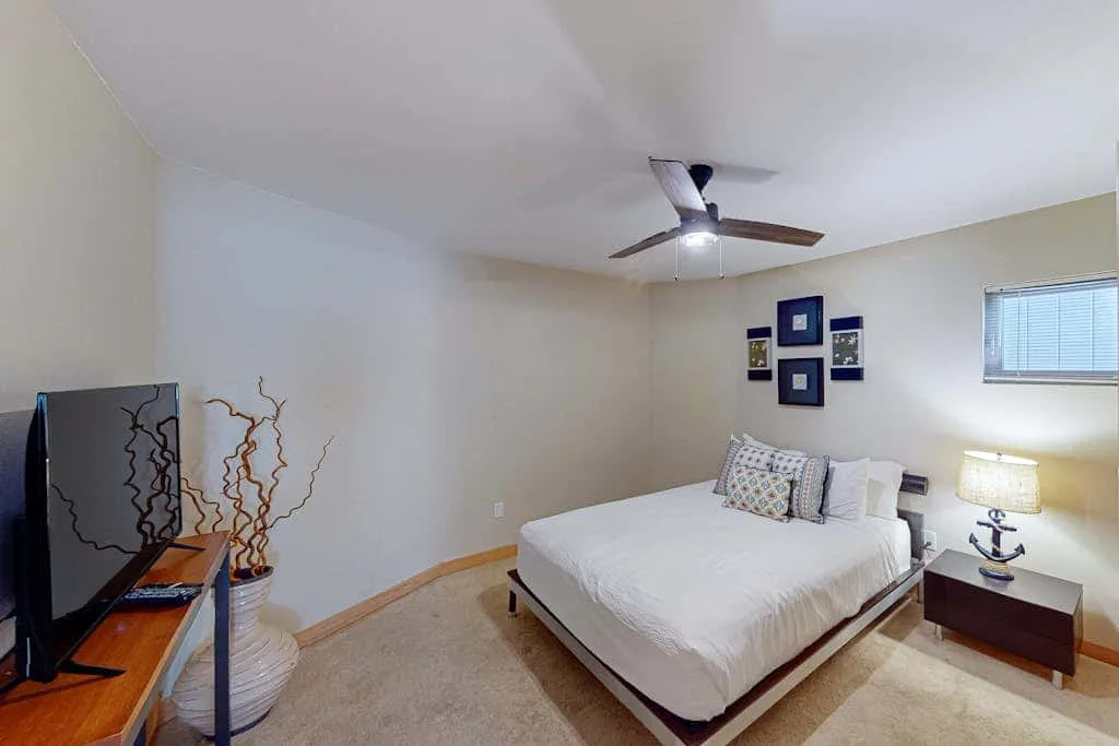 A bedroom with a neatly made bed, wall art, and a ceiling fan.
