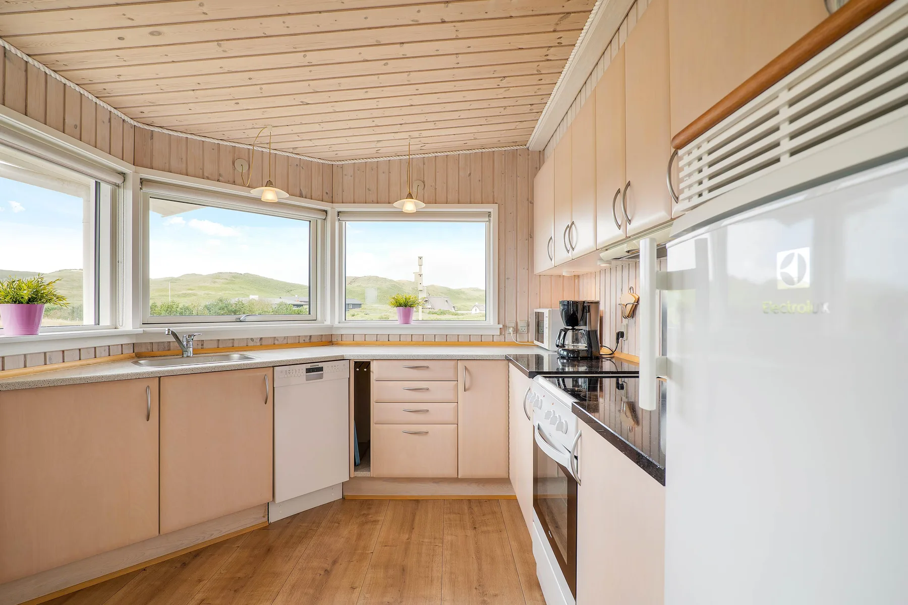 Una cocina luminosa con gabinetes de madera, encimeras y ventanas con vistas a colinas verdes.