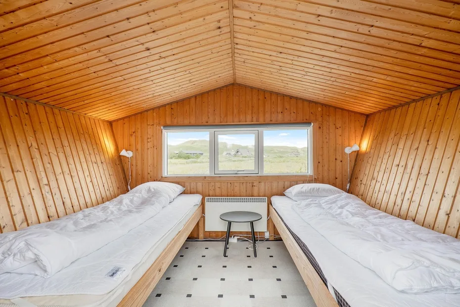 Un dormitorio revestido de madera con dos camas y una ventana con vistas a terreno abierto.