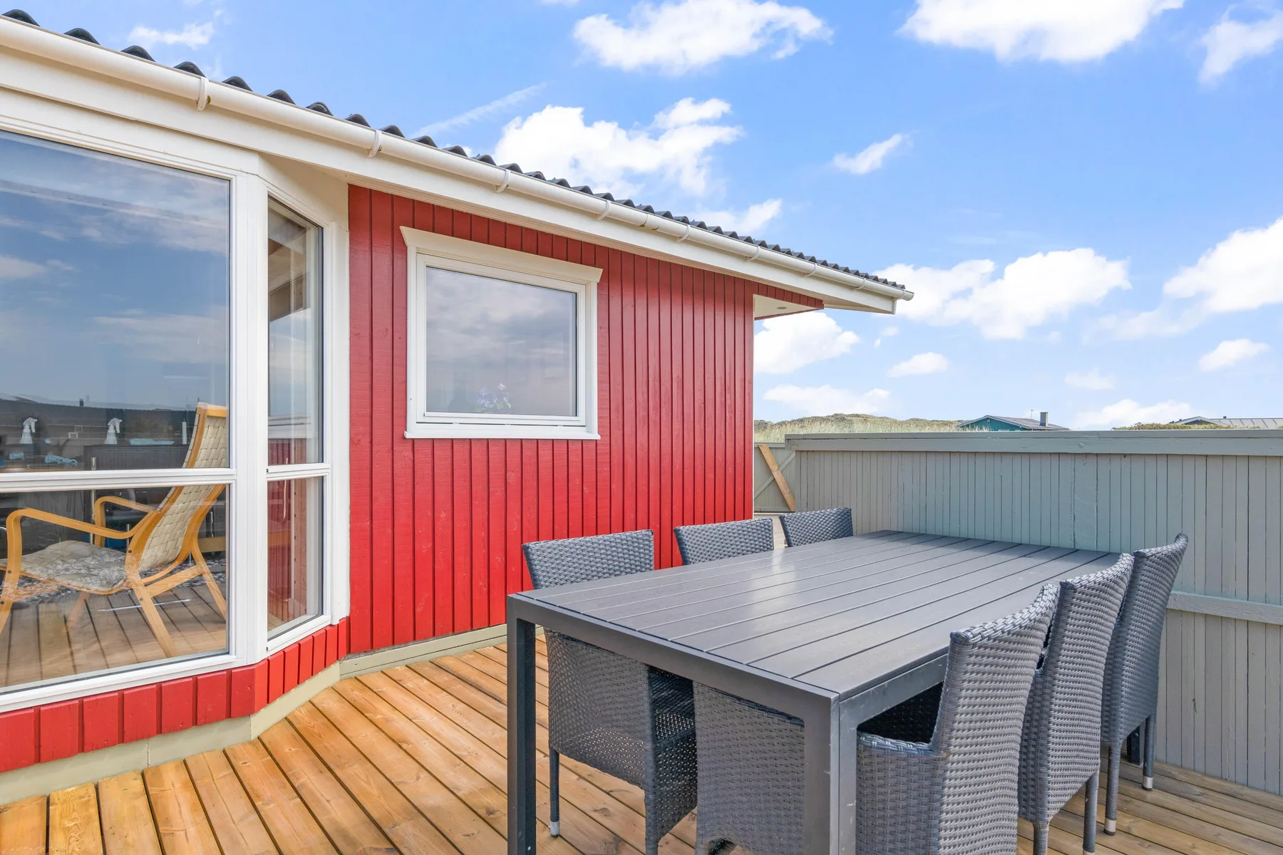 Una terraza de madera con asientos al aire libre junto a una casa roja.
