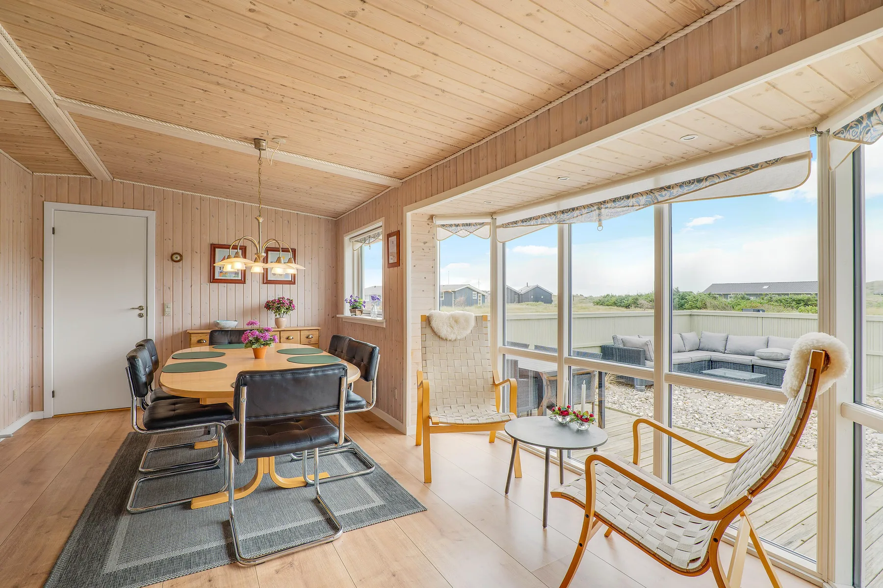 Una sala luminosa con mesa de comedor y asientos junto a grandes ventanales.