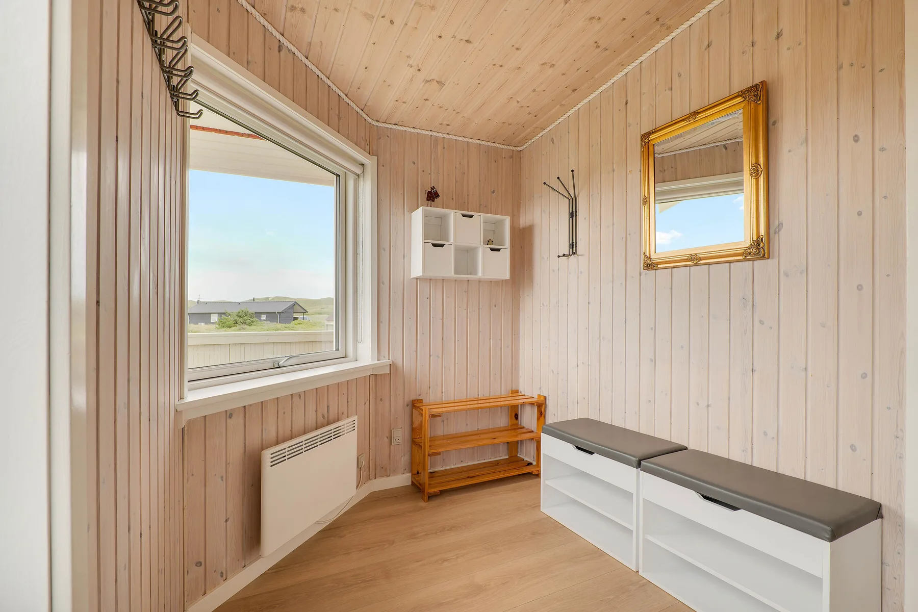Una pequeña habitación revestida de madera tiene una ventana, un espejo y asientos tipo banco.