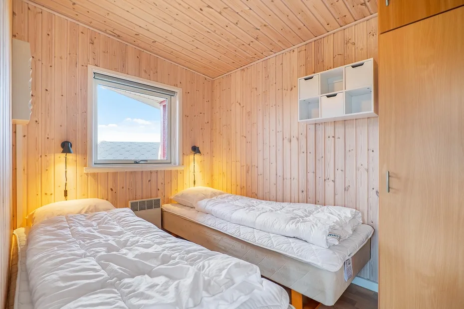Un dormitorio revestido de madera con dos camas y una ventana con vistas al agua.