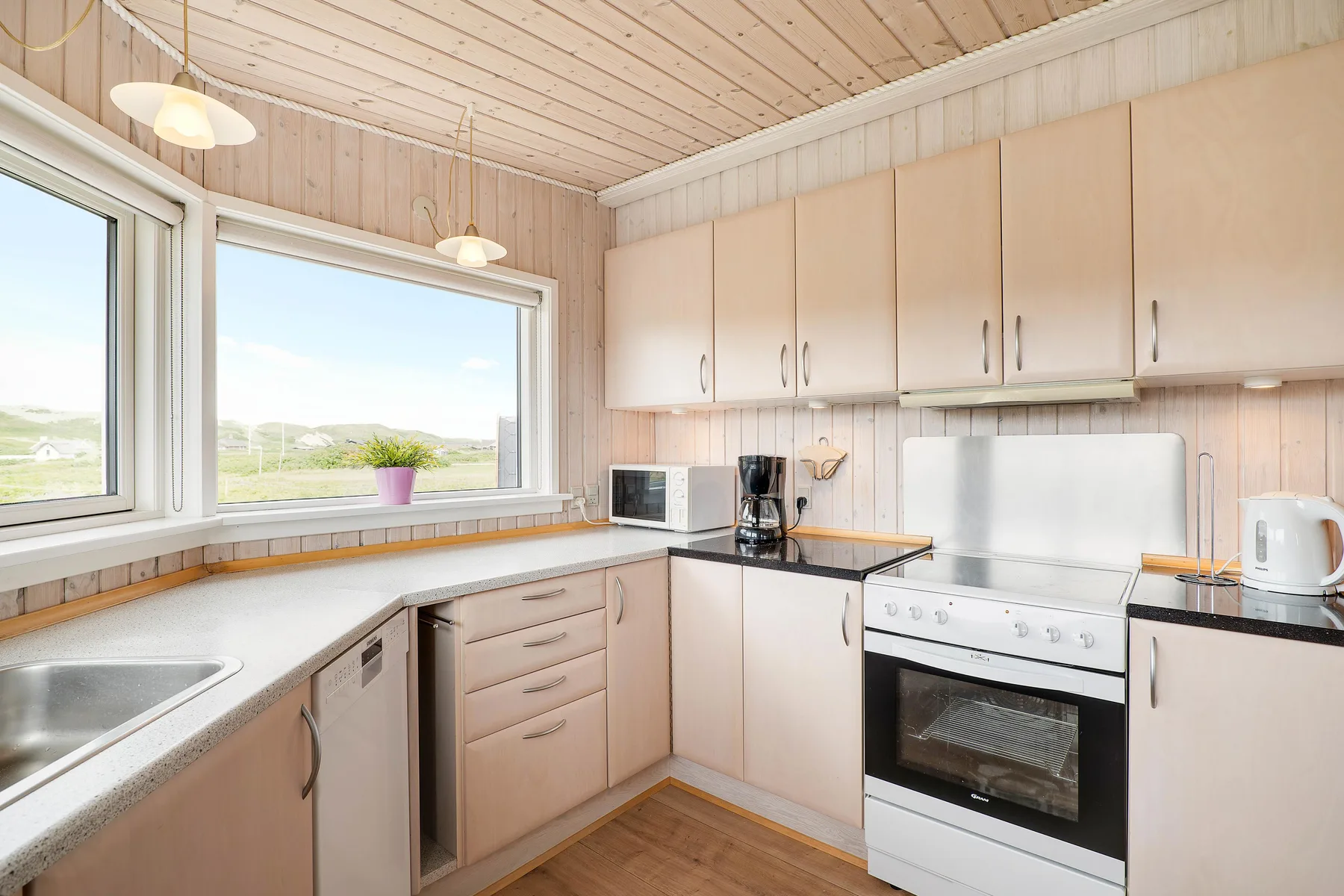 Una cocina luminosa con gabinetes claros y una encimera bajo dos ventanas.