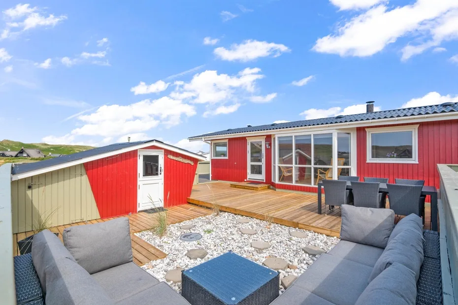 Una casa roja da a una terraza de madera y una zona de asientos al aire libre.