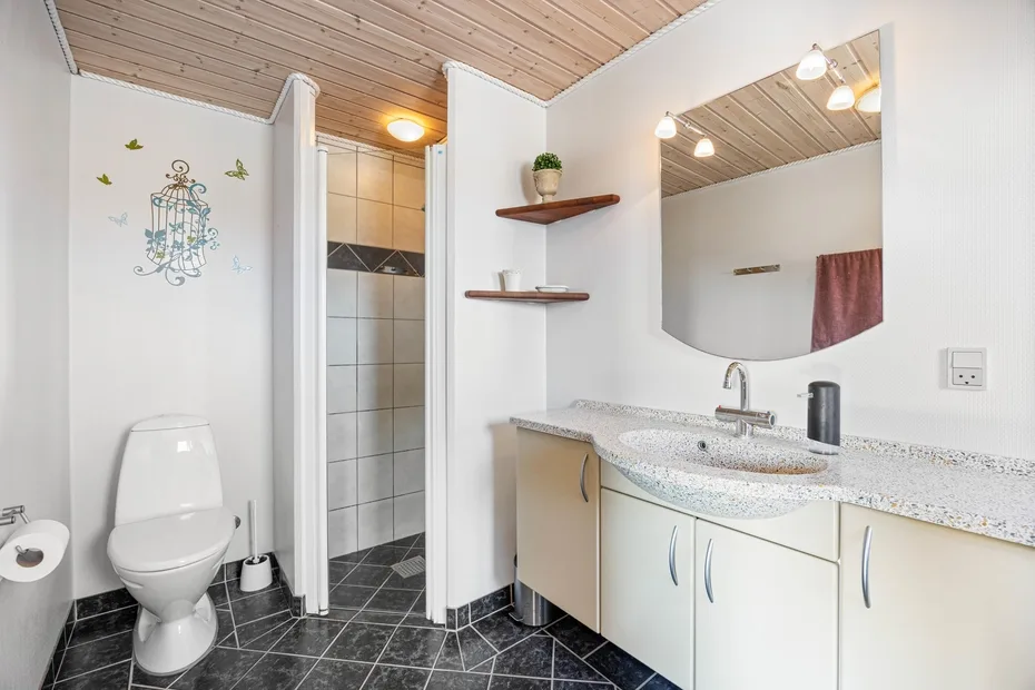 Un baño con mueble de lavabo, espejo de pared, inodoro y zona de ducha con azulejos.