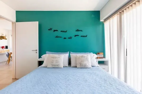Dormitorio con una cama junto a una pared verde azulado y cortinas junto a la ventana.