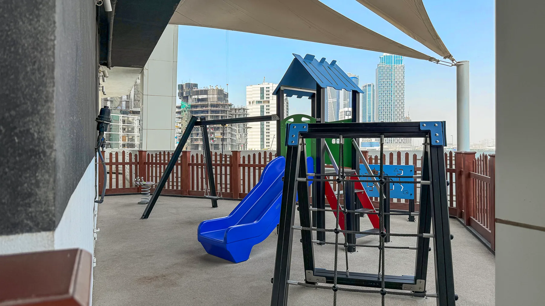 Un parque infantil al aire libre con un tobogán azul y una estructura para trepar está bajo una cubierta.