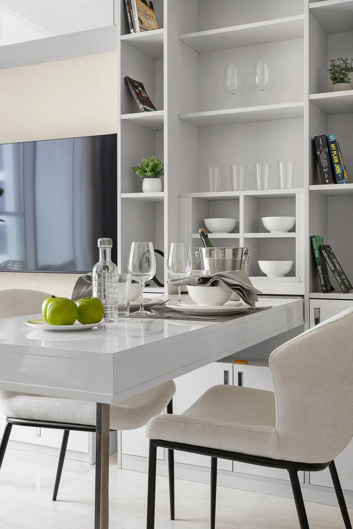 Un comedor luminoso con la mesa puesta y estanterías blancas empotradas.