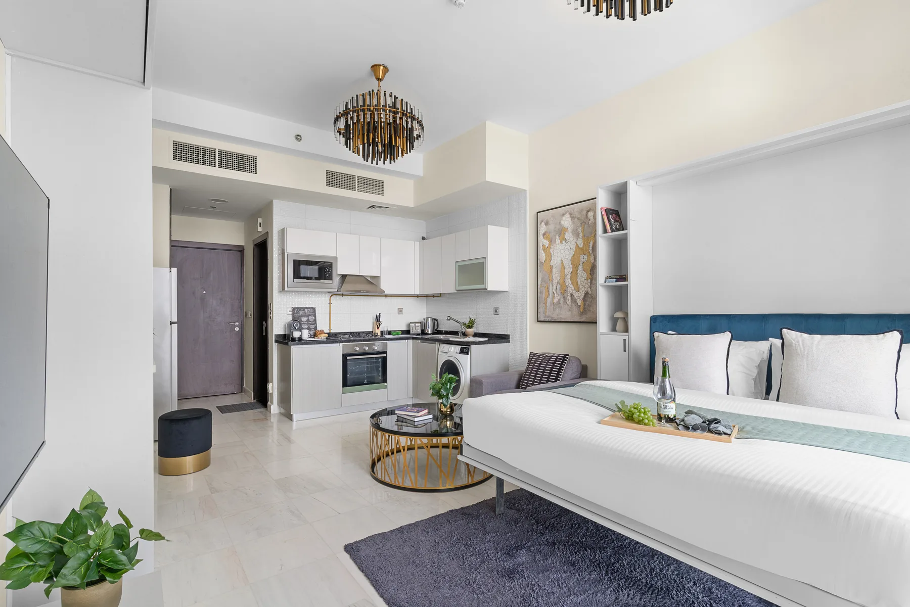 Un dormitorio luminoso con cama, zona de estar y cocina compacta.