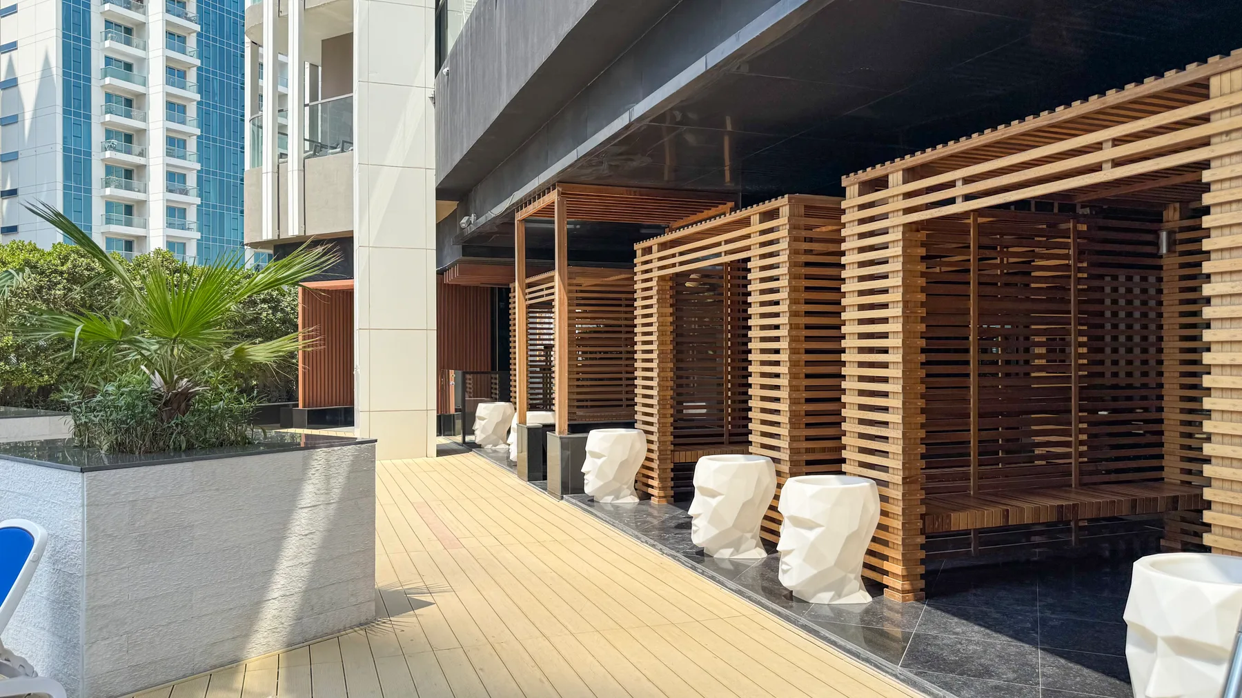 Un pasillo exterior moderno bordea estructuras de listones de madera y vegetación.