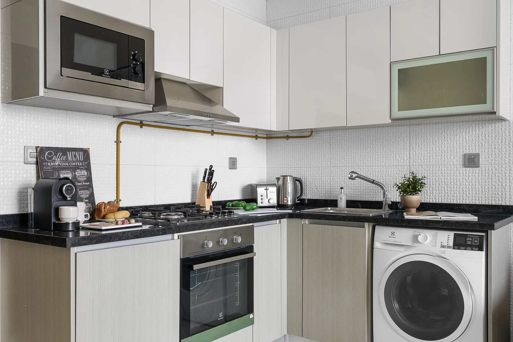 Una cocina moderna con microondas, electrodomésticos sobre la encimera y una lavadora.