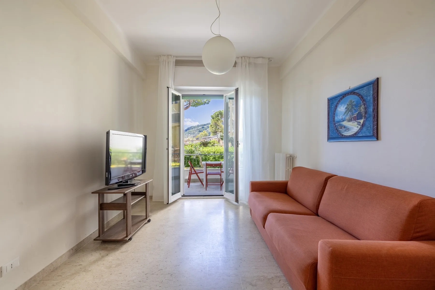 Una sala luminosa con televisor y sofá junto a una puerta abierta al balcón.