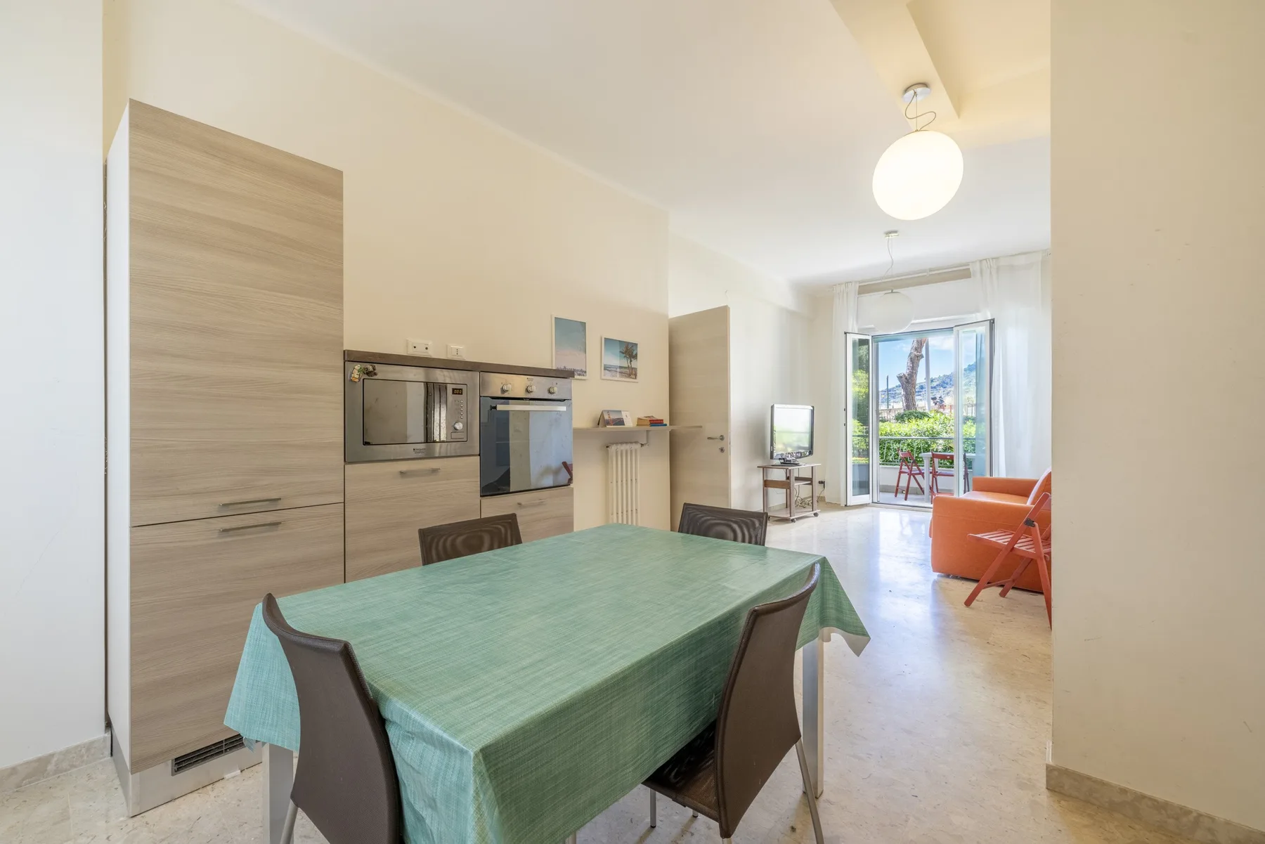 Comedor con una mesa cubierta de verde junto a la cocina y una luminosa zona de estar.