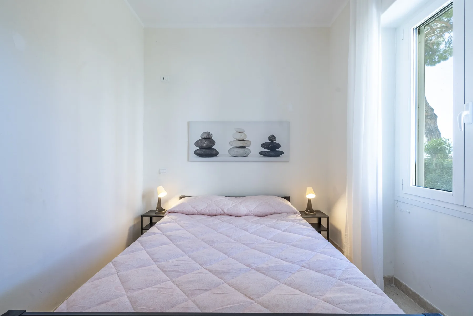 Un dormitorio con una cama bajo un cuadro y una ventana.