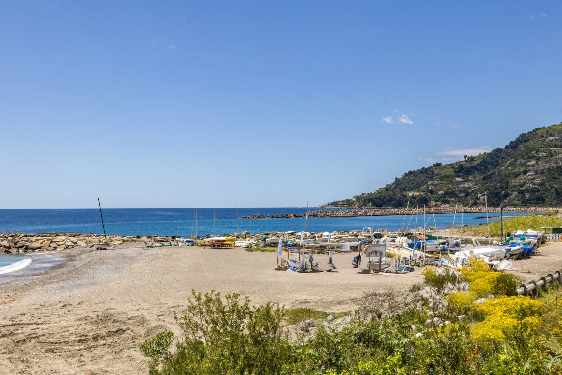 Una playa de arena y pequeñas embarcaciones bordean la costa bajo una colina verde.