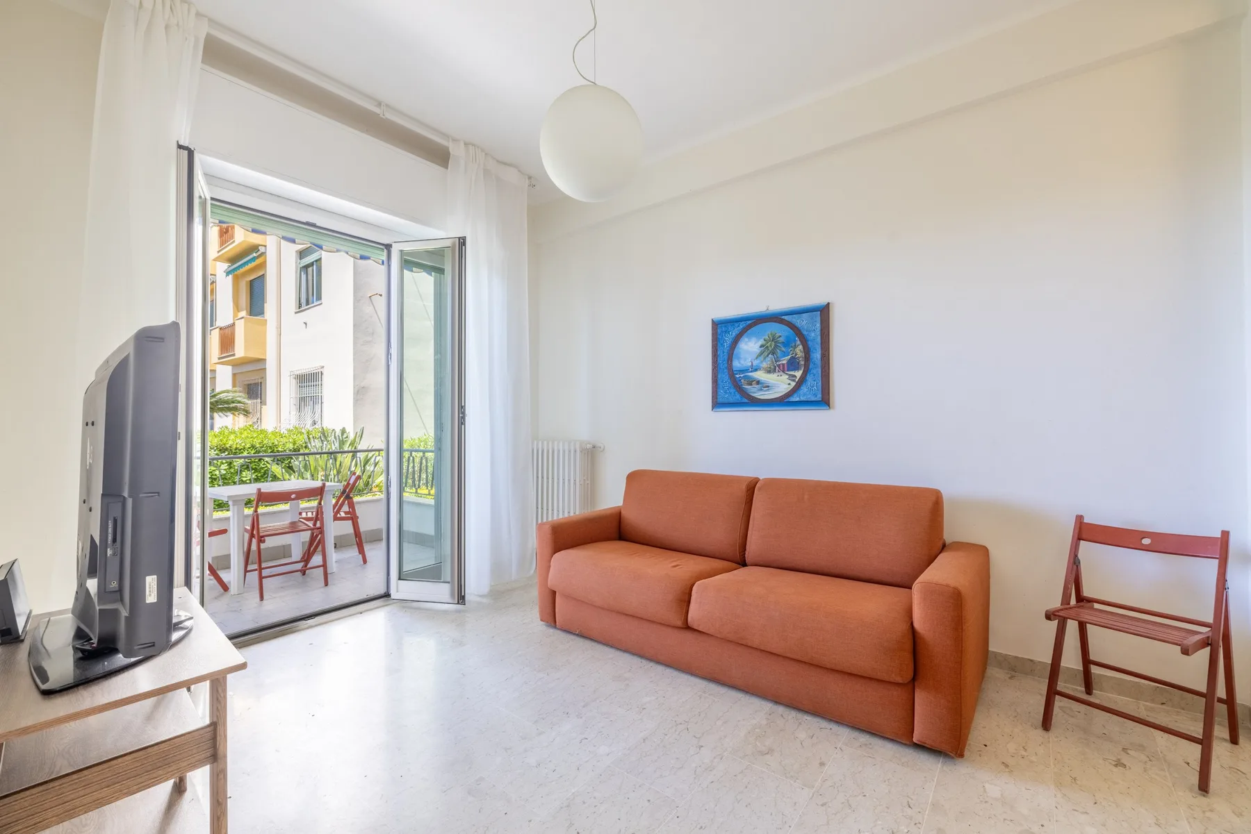 Una sala luminosa con asientos naranjas y una puerta corrediza abierta hacia un balcón.