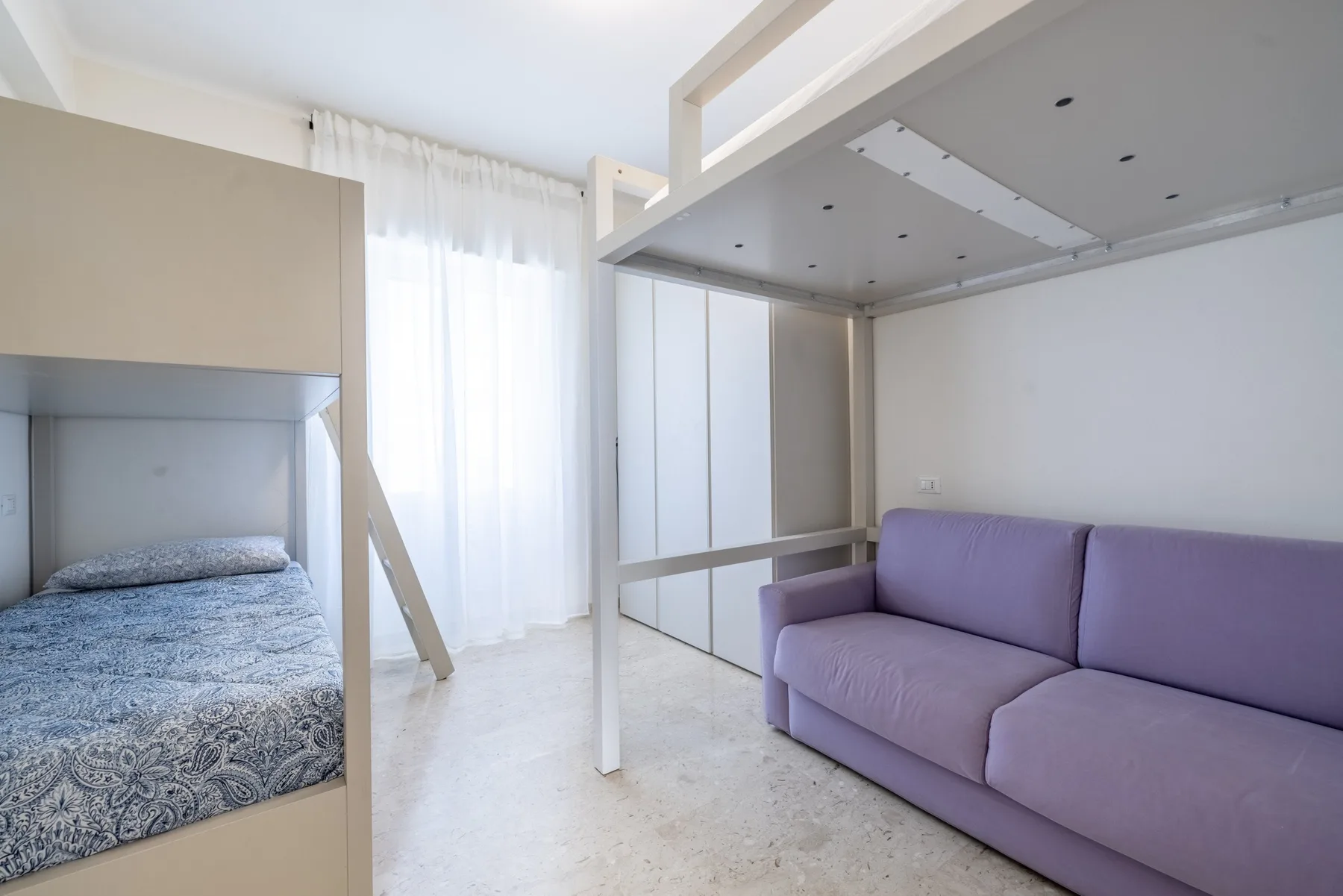 Un dormitorio luminoso con una cama elevada sobre un sofá morado.
